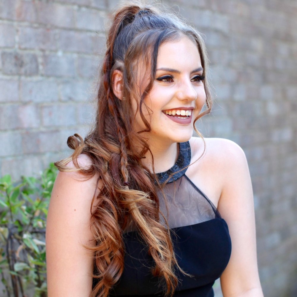 Teen girl smiles in black prom dress with a high half updo and curls