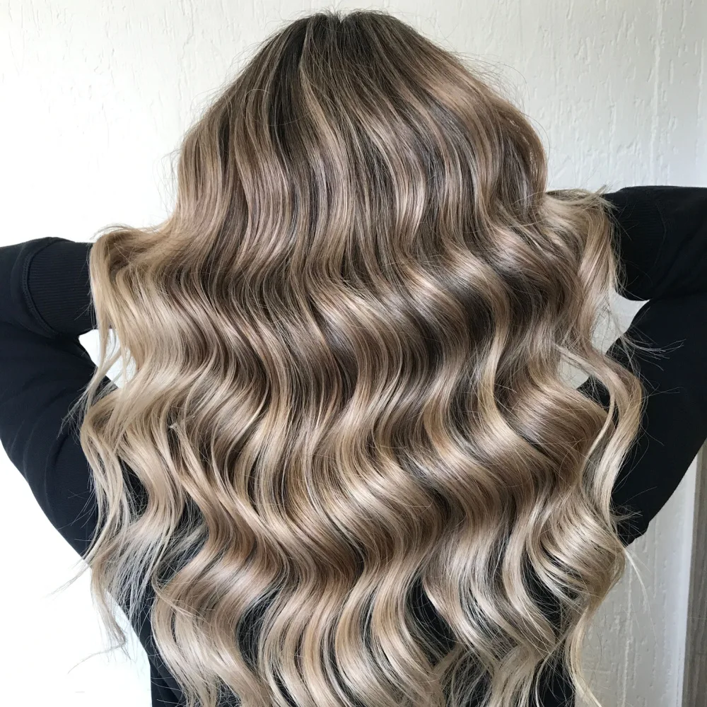 Back view of woman in black long sleeves holding up her wavy dirty blonde hairstyle with highlights