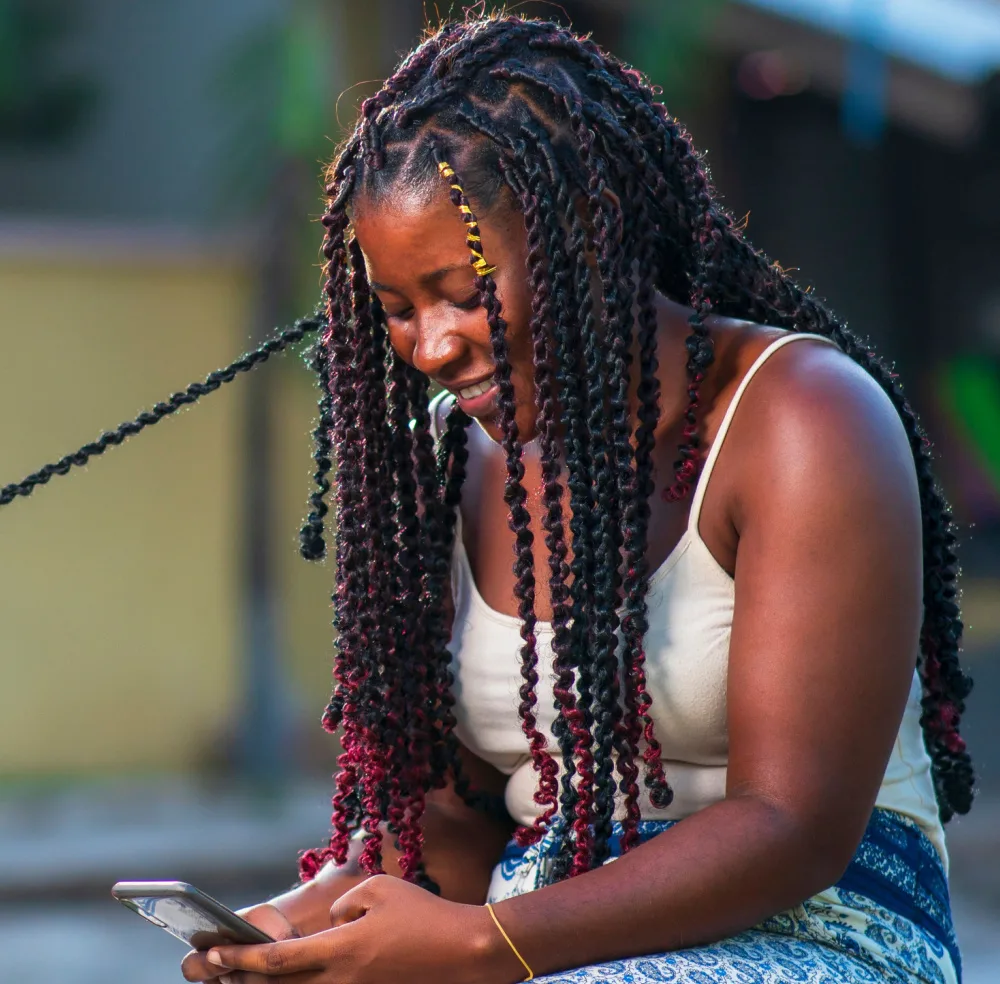African American woman smiles down at her phone while she tries spring twists, one of the top cute black hairstyles