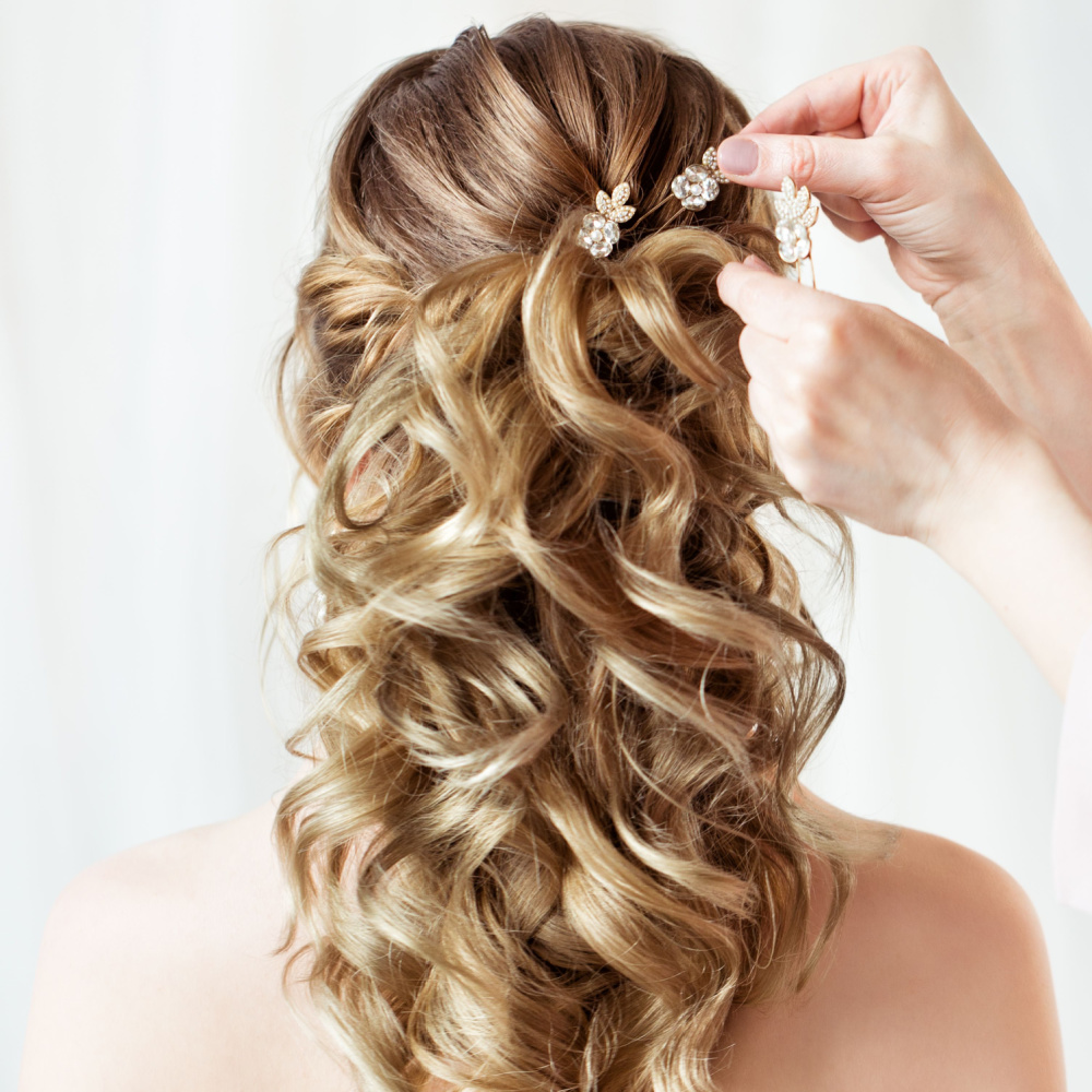Back view of blonde formal half up prom hairstyle with flower pins and curls