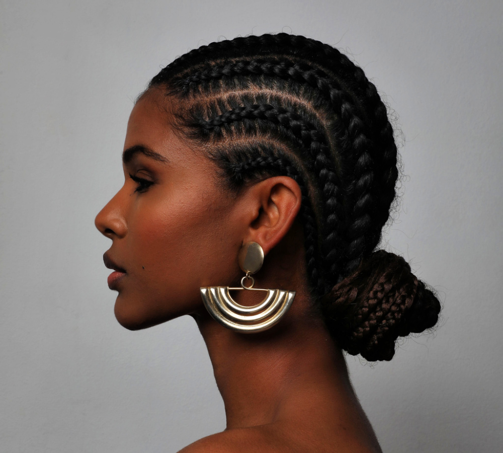 African American woman seen from the side wears thick cornrows with a low bun hairstyle and big earrings