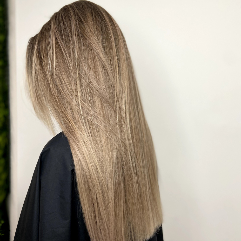Side rear view of model with freshly dyed straight hair in a dirty blonde color wearing a black salon cape
