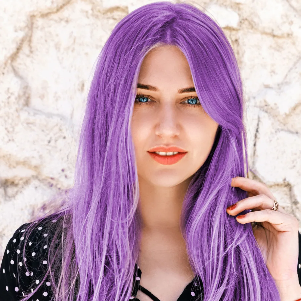Woman touches her long lavender hair in front of a stone wall with a black polka dot shirt on