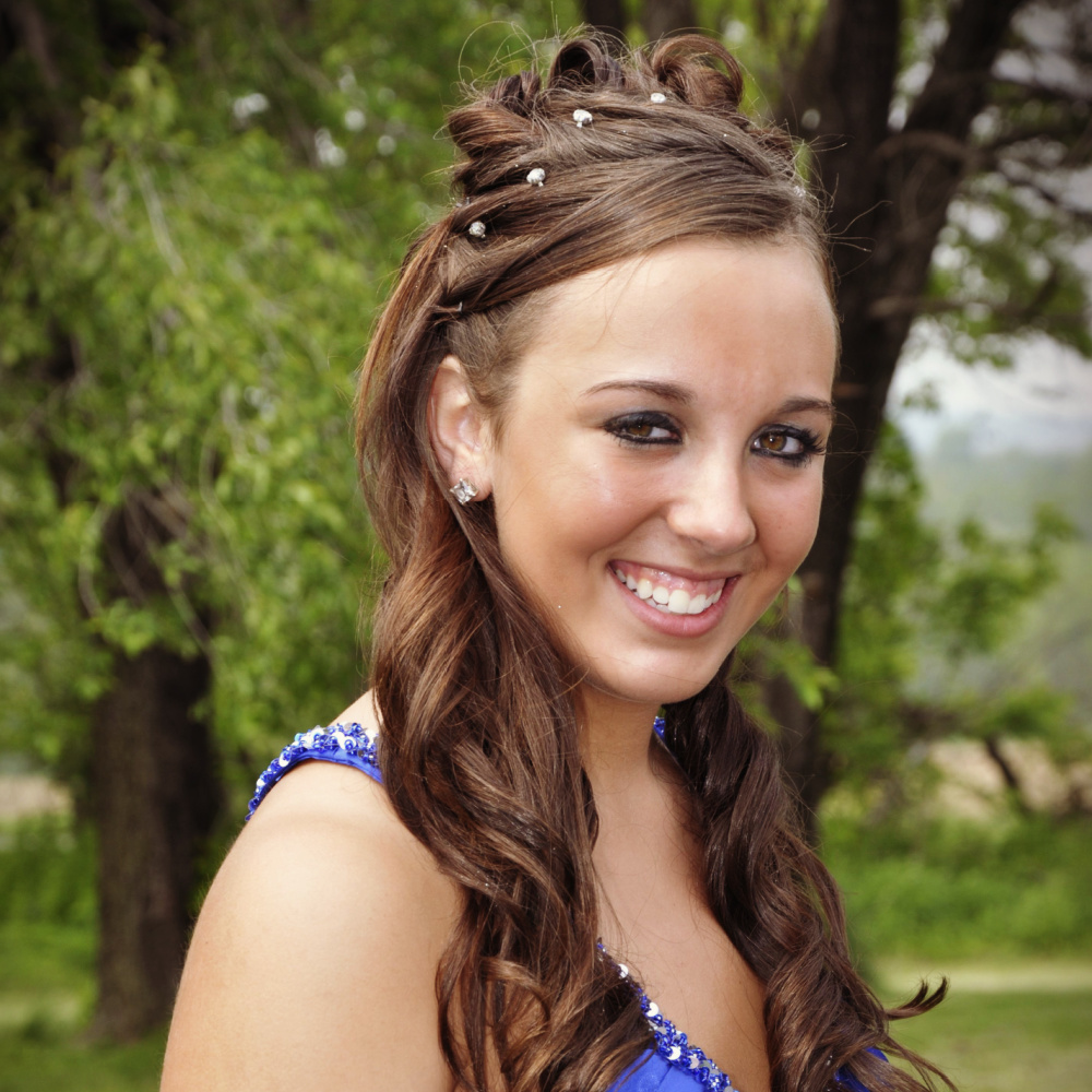 Brown haired teen girl in blue dress wears one of the trendy half up prom hairstyles with pins and curls