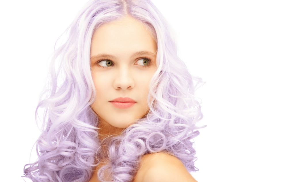 Close up of woman with long curly lavender blonde hair styled with a middle part in front of a white background