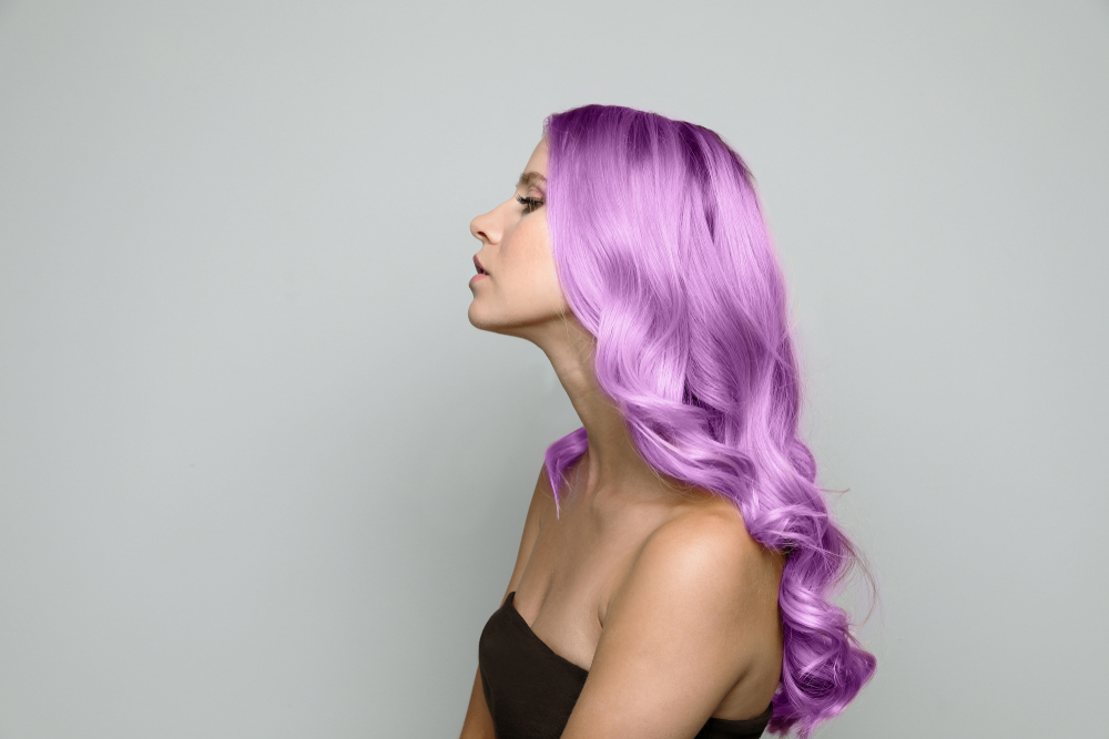 Woman in a black strapless top faces the side and closes her eyes with long bright lavender hair styled in curls 
