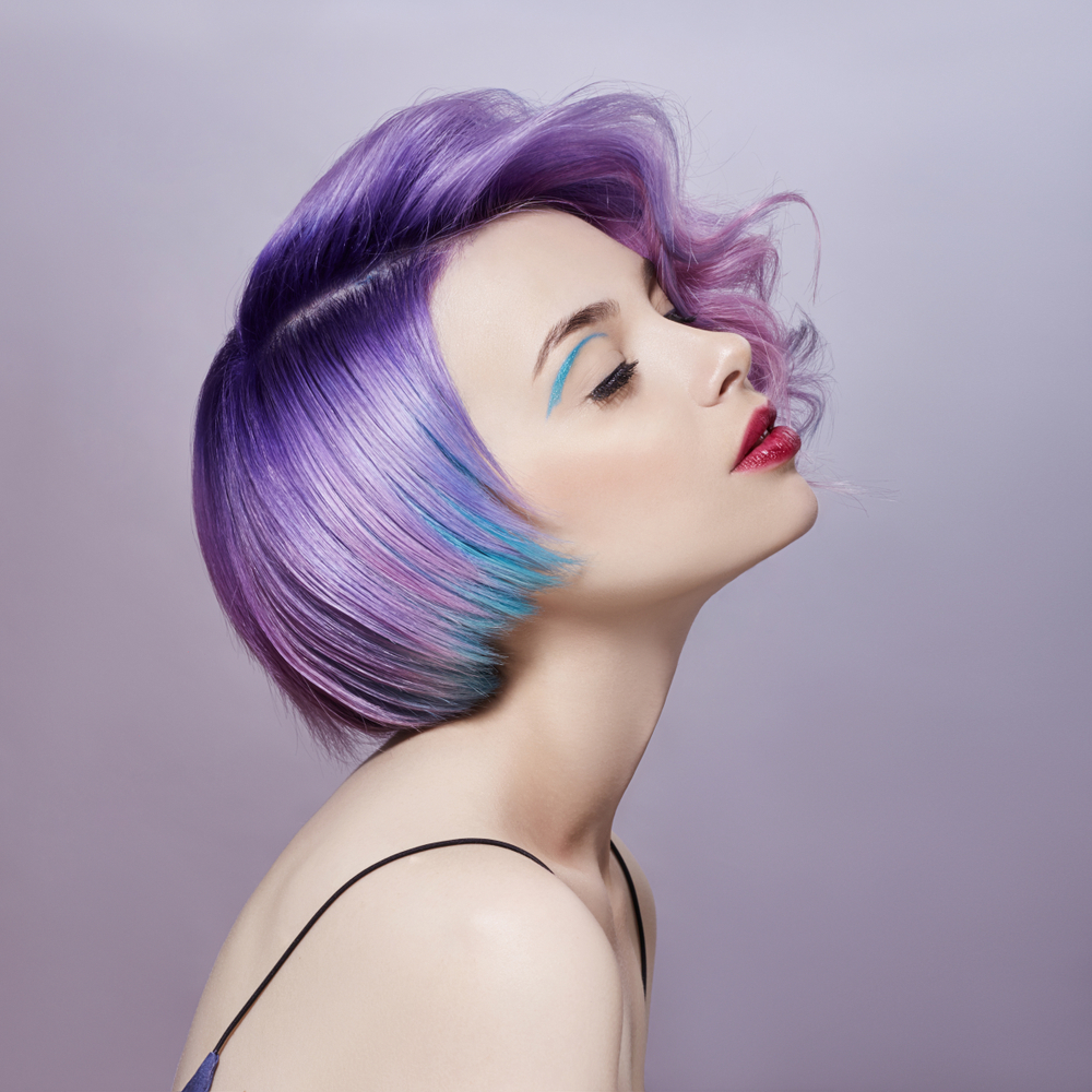 Woman viewed from the side with purple and blue hair wears a spaghetti strap top with closed eyes and head tilted up