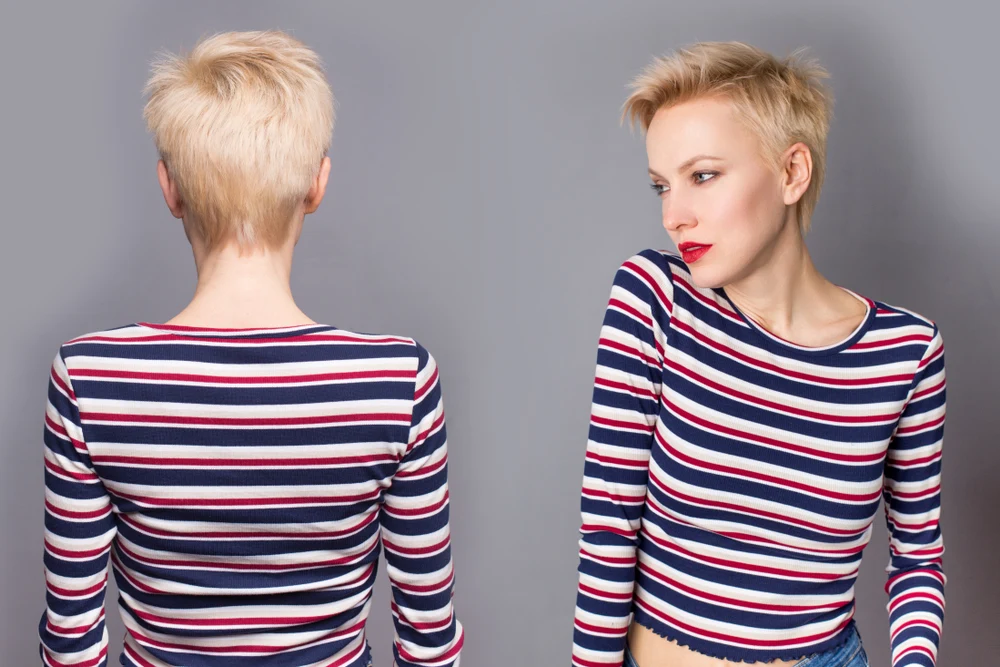 Blonde woman with short hair wears a striped red and blue shirt in front of gray wall to show how she's styling a short pixie cut