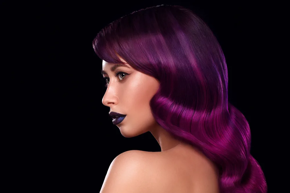 Side profile view of woman wearing plum hair color with fuchsia ribbon balayage against a black background