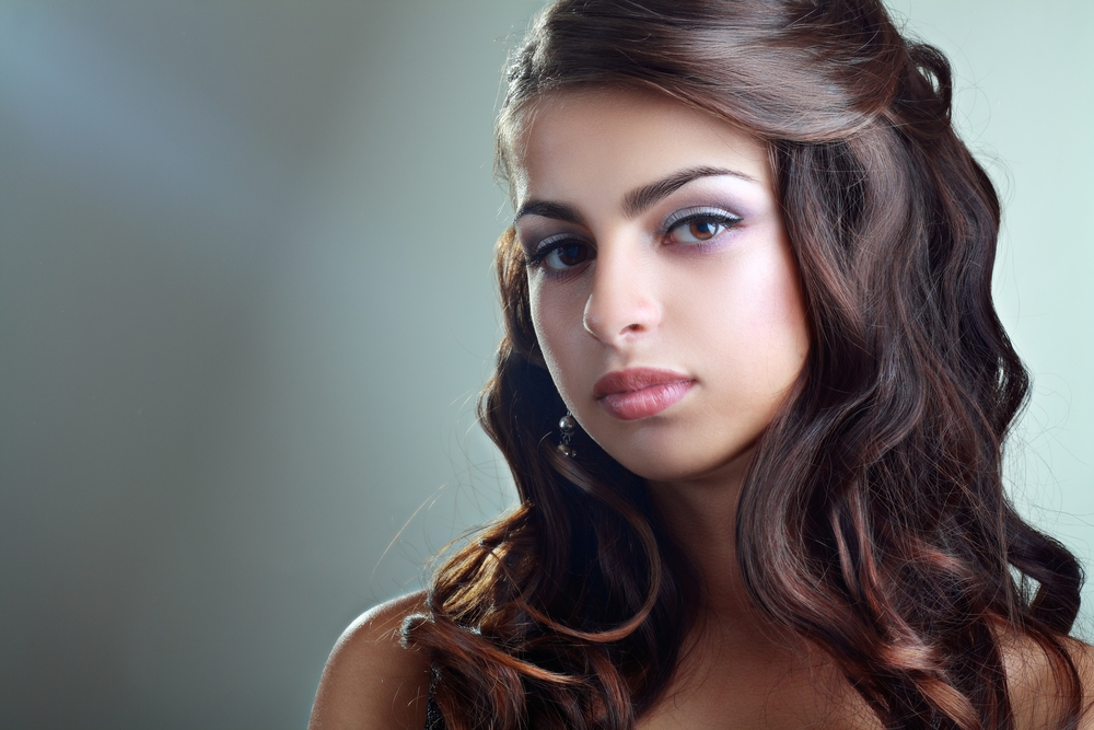 Young brunette girl wears a formal prom hairstyle with side-swept hair half up and soft waves
