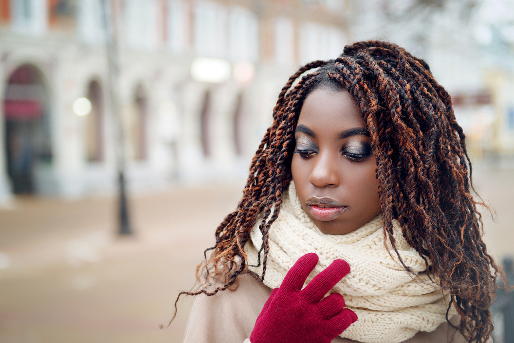 African American girl with spring twist hair wears a coat, scarf, and red gloves outside walking the city