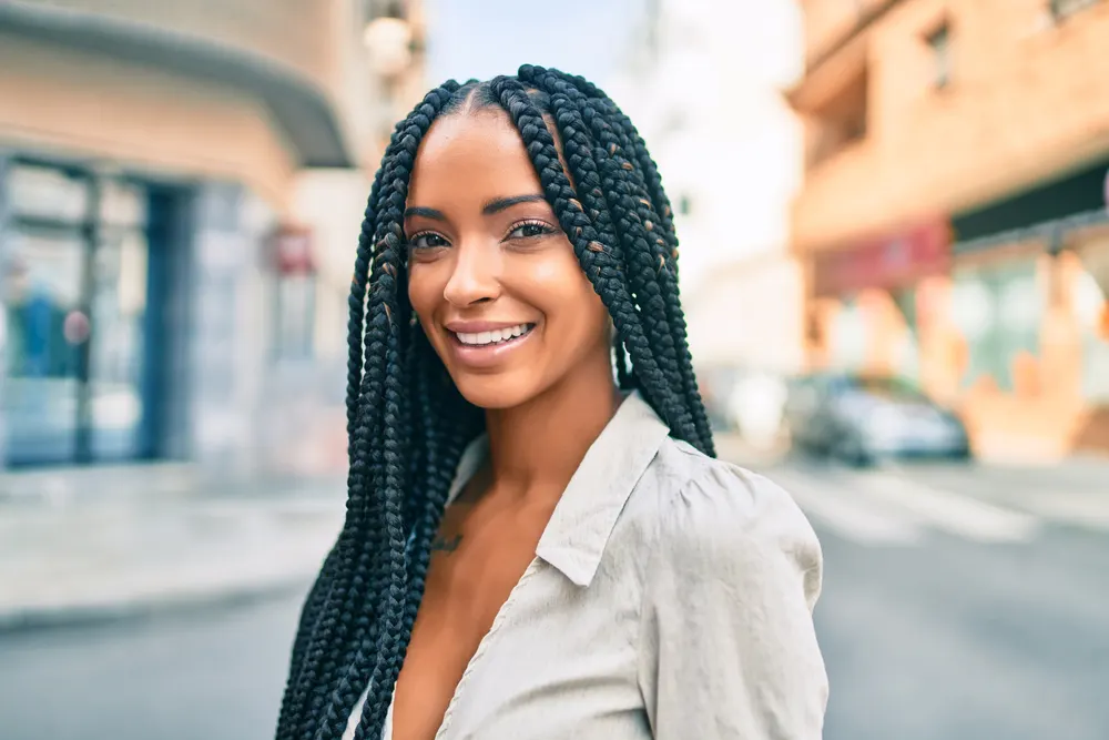 Smiling young black woman walks a city street with box braids hairstyle and a light blazer on