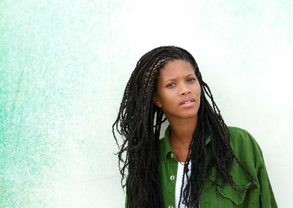African American woman with long spring twists wears a side part with a green button down shirt in front of gradient green background