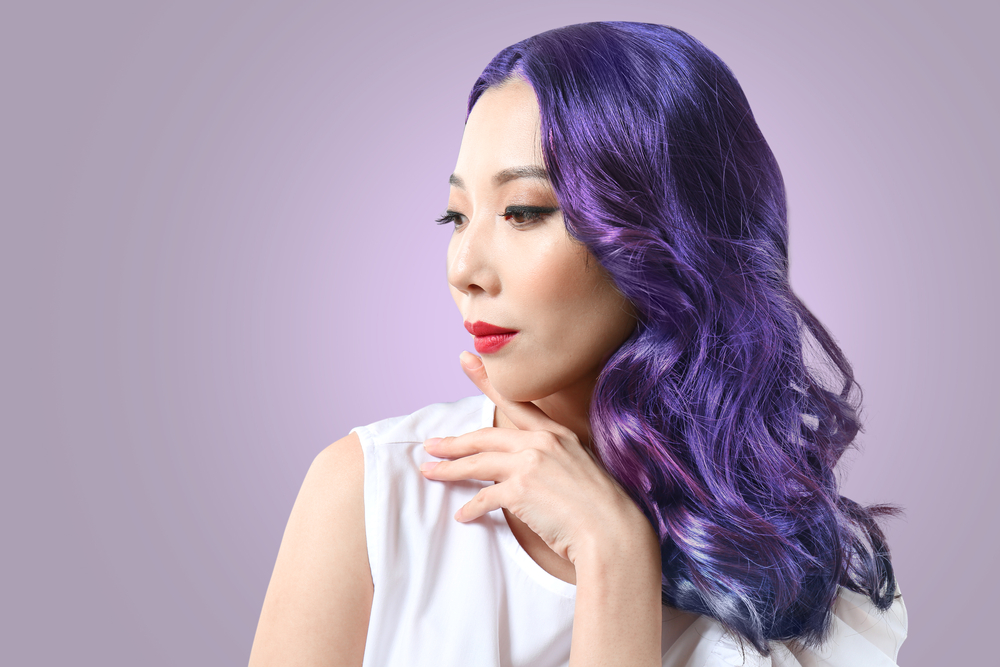 Asian woman looks to the side with hand rested under her chin to model long wavy lavender hair