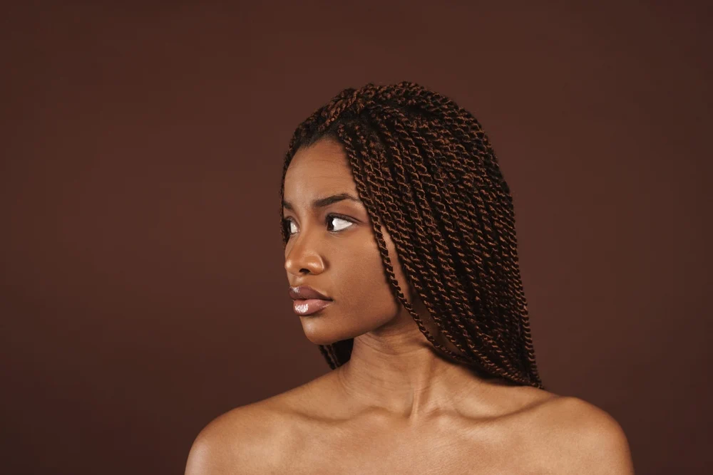 African American girl with bare shoulders looks away with her copper and brown spring twist hair behind her shoulders