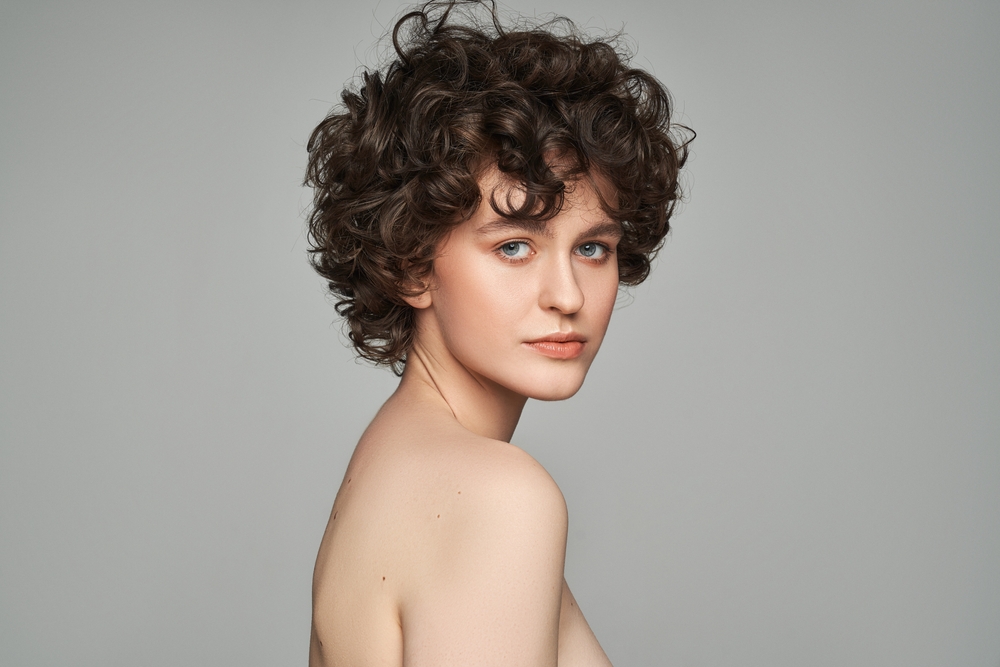 Portrait of a woman with pale skin looking over her right shoulder and wearing a fluffy and short tomboy haircut