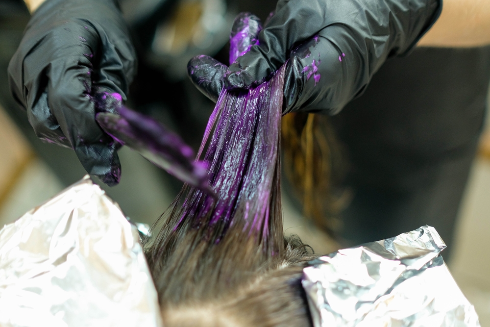 Woman getting her hair dyed purple in a studio by a gloved hairdresser