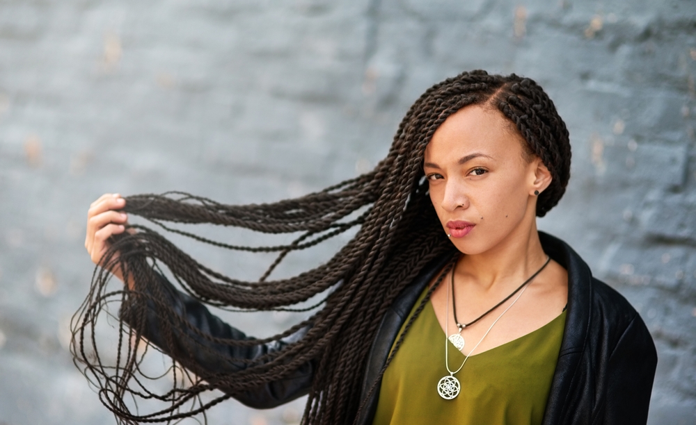 Woman in green shirt and black cardigan holds out her long hair to show off the Senegalese twists hairstyle