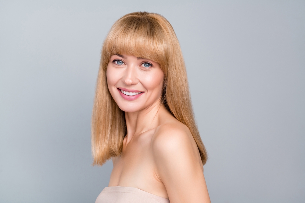 Woman with a round face and bangs pictured smiling in a studio and looking at the camera