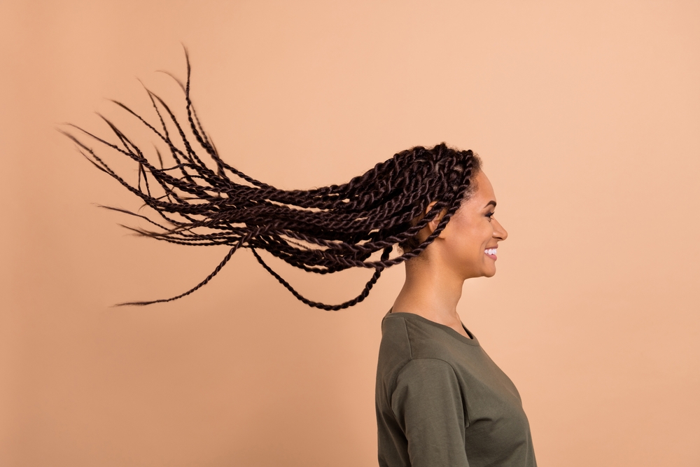 Mixed woman side view with spring twist hair lifted up to show the texture in front of peach-colored wall