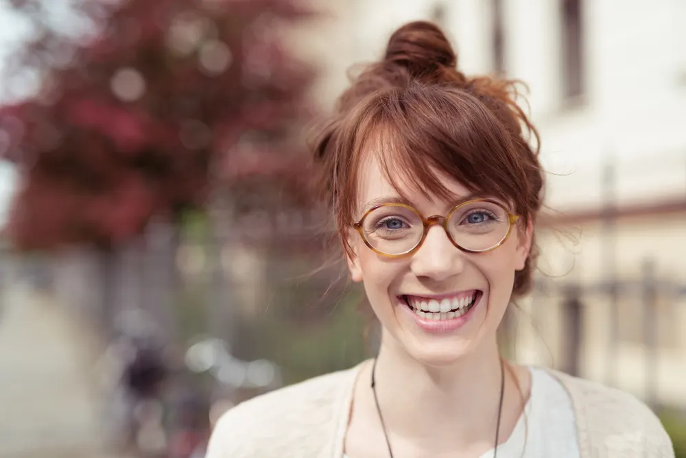 Messy Top Knot With Layered Side-Swept Bangs on a woman smiling big with a blurred background