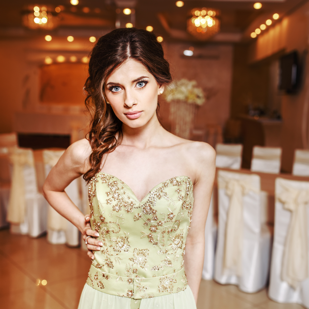 Girl with green prom dress shows off her formal half up hairstyle draped over one shoulder with her hand on her hip