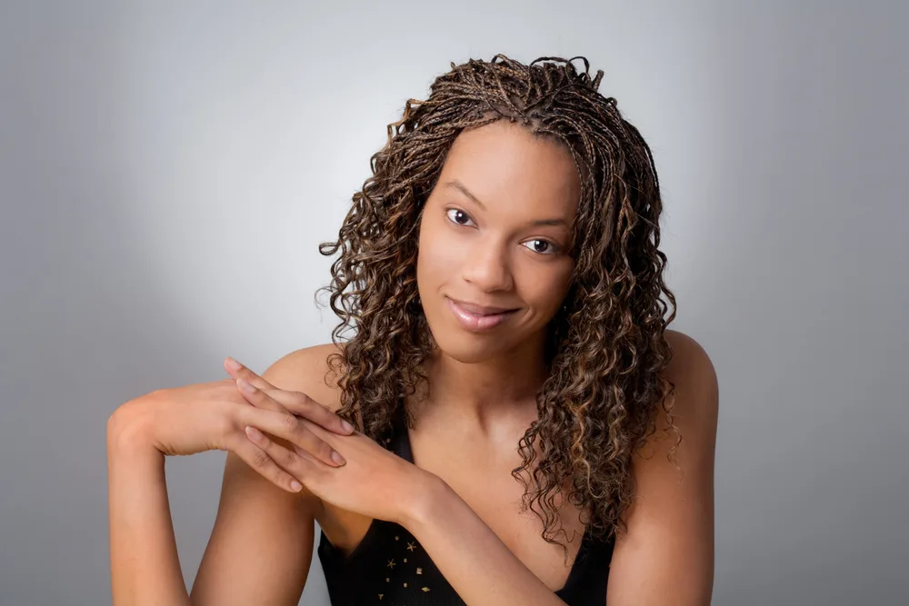 African American woman holds hands together in a black tank top with curly micro braids as one of the top cute black hairstyles