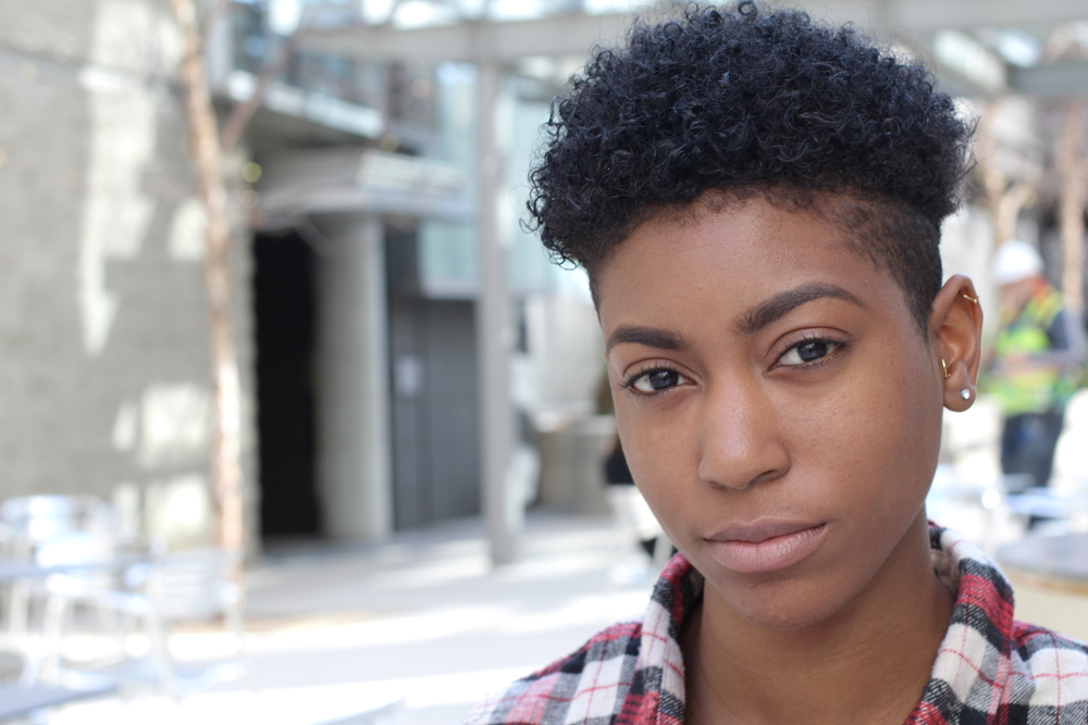 Serious African American woman looks at the camera with a short mid undercut and plaid shirt on a city street for a piece on the new Brittney Griner haircut style