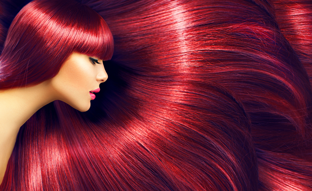 For a piece on purple and red hair colors, a woman with fair skin lets her red hair fan out on the right side of the image while also looking right