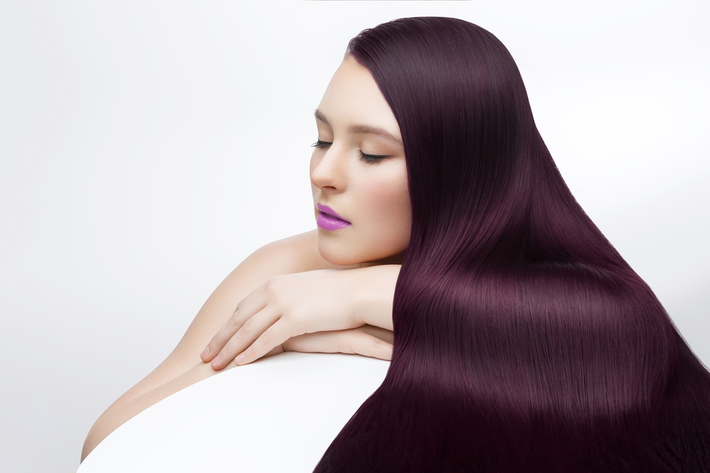 Woman lays down with her plum hair spread out in front of her over her folded arm in front of a white background