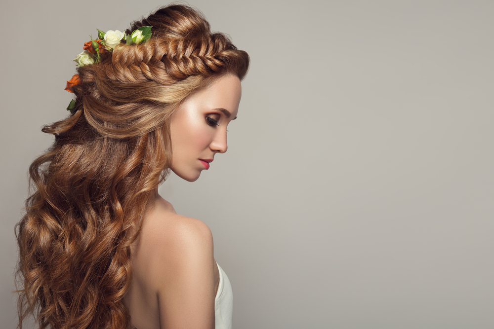 Woman side view shown looking down wearing an example of intricate fishtail half up prom hairstyles