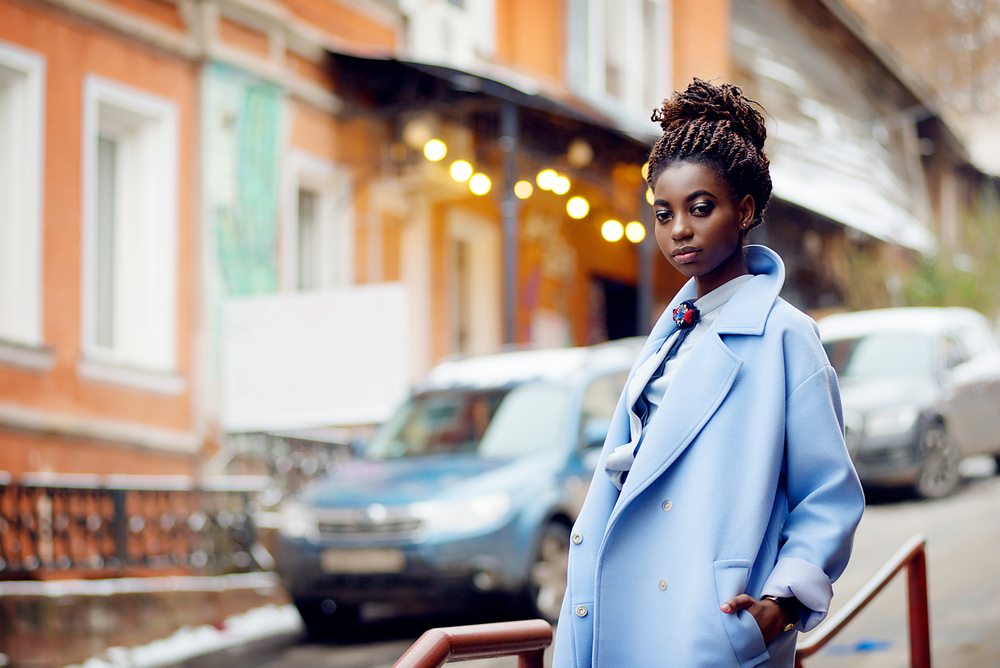 African American woman on city street wears a chic blue coat with twisted bun hairstyle