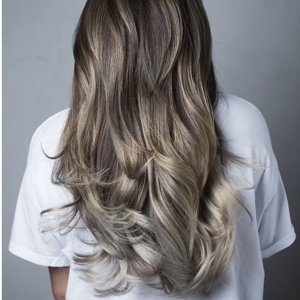 Close-up of a woman in a white t-shirt with long, curled grey ombre hair with brown, blonde, and grey tones 