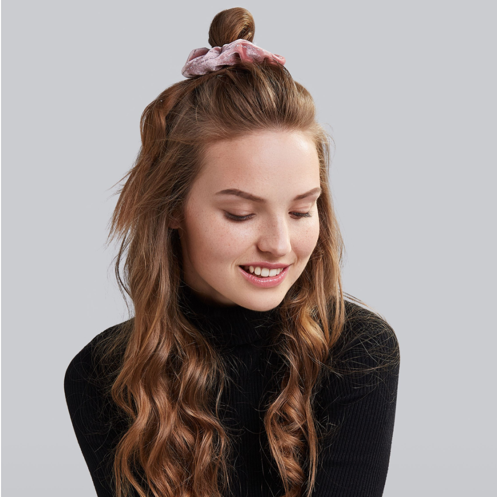 Young woman glances down with a black turtleneck top and her curly hair styled in a half-up top knot with a scruncy