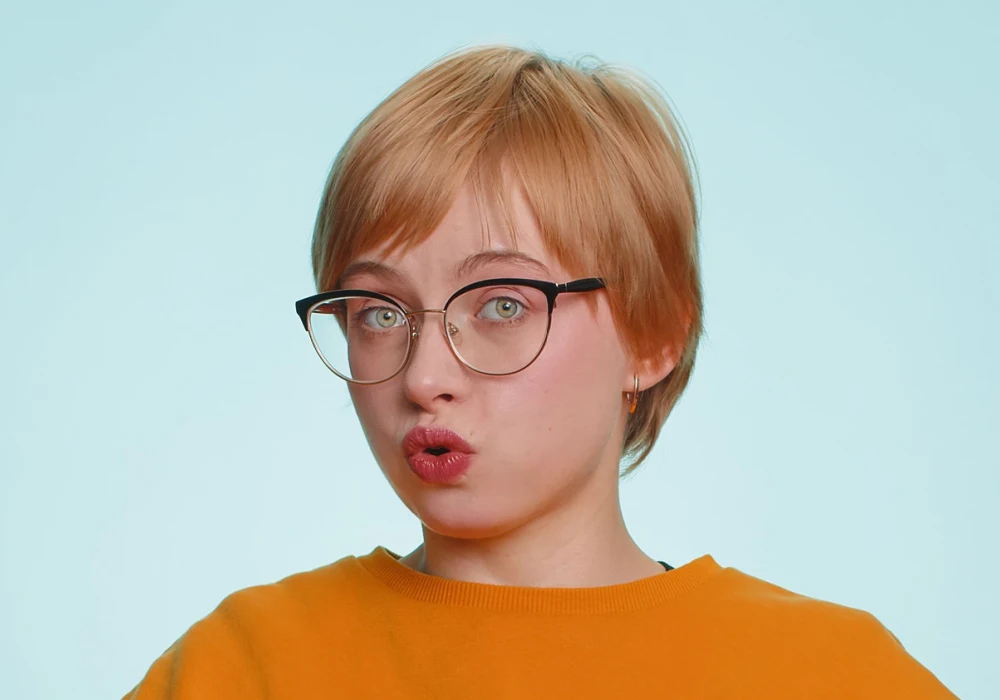 Red-haired woman in an orange shirt sports a sleek pixie crop parted to the side, which is one of the most flattering short haircuts for oval faces