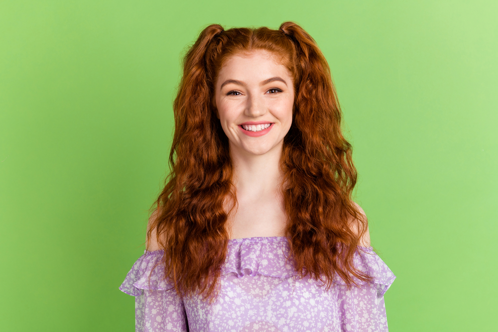 Woman in purple shirt wears her curly red hair in high pigtails that fall over her shoulders, shown as an example of cute hairstyles for curly hair