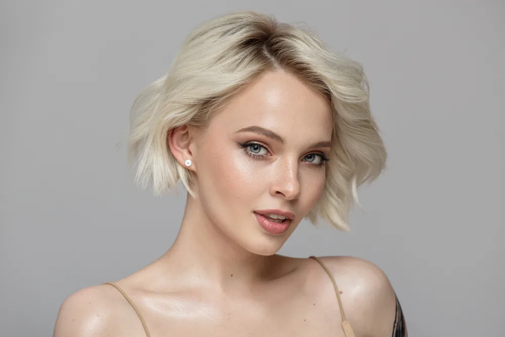 Woman with bare shoulders and blonde wavy hair rocks a short bob with textured layers parted to the side as one of the best short haircuts for oval faces