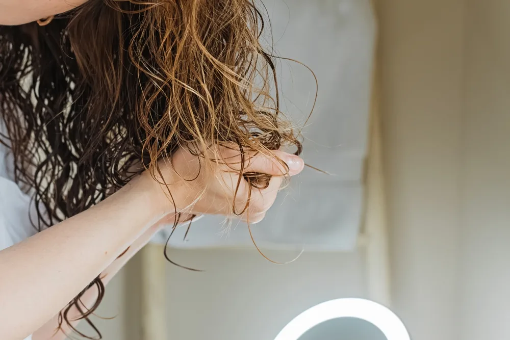 Unrecognizable woman leans over to scrunch her curly hair while it's wet for a piece listing lots of cute hairstyles for curly hair