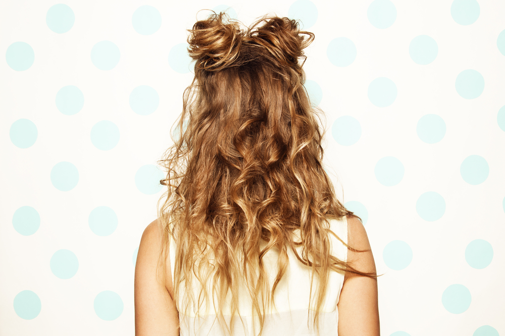 Rear view of woman wearing one of the many cute hairstyles for curly hair featuring half up space buns