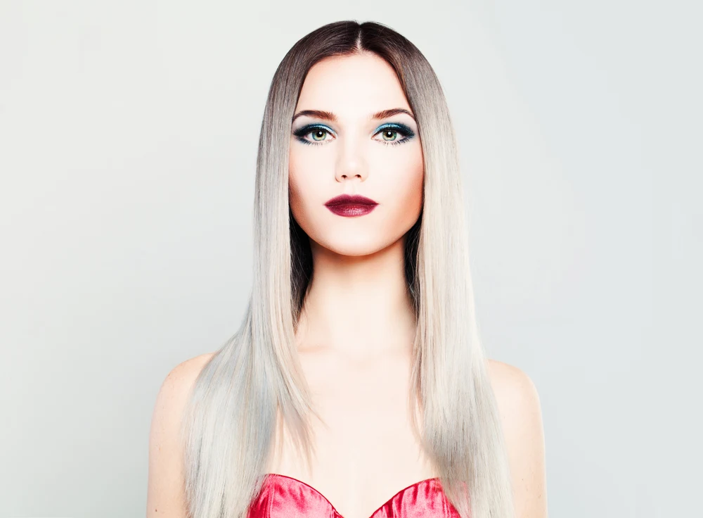 Woman looking straight on has dark red lipstick with long brown to grey ombre hair color styled in a middle part