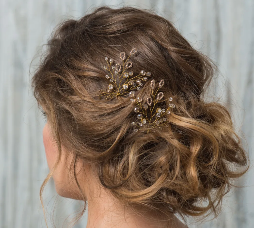 Brunette woman seen from the back side has a curly low updo with jewel accents perfect for homecoming or prom