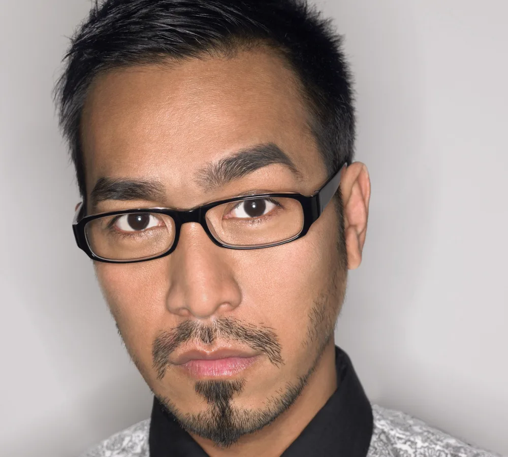 Young Asian man wearing glasses and a collared shirt shows off a popular goatee style, the Balbo goatee, with stubble on the cheeks