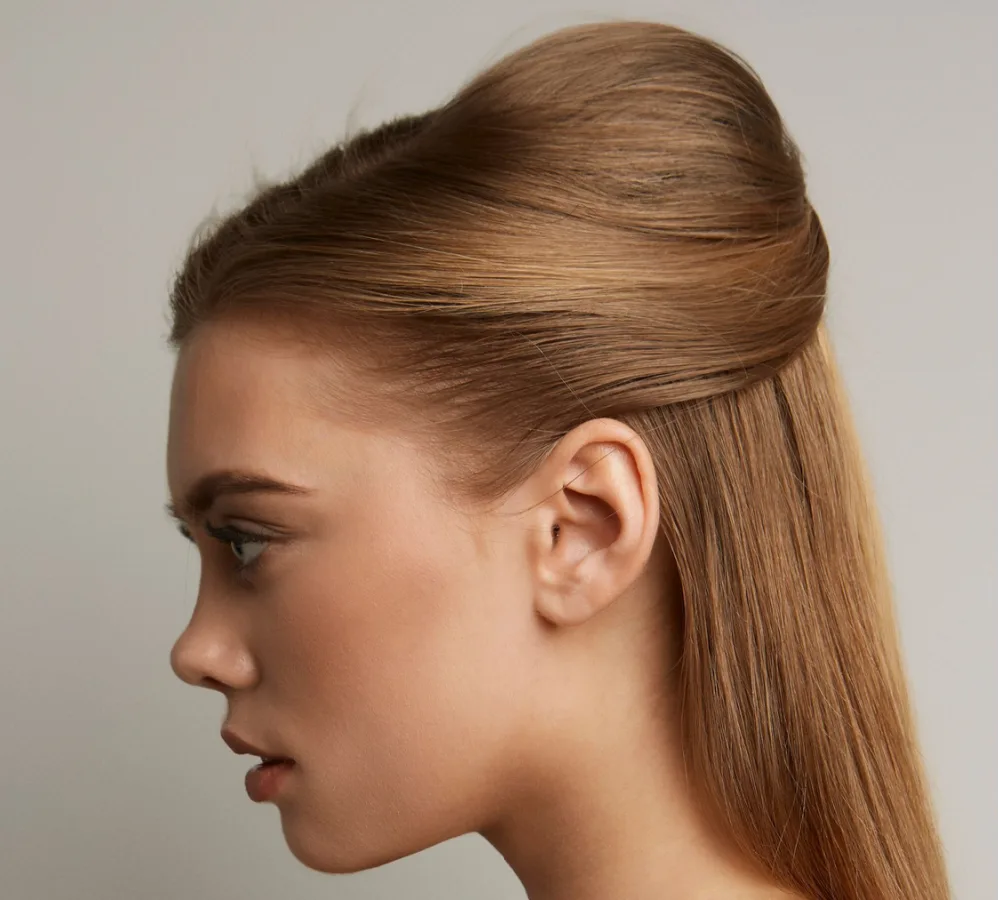 Profile view of woman with a half updo and volumized crown in front of a gray wall to show hairstyles for long straight hair