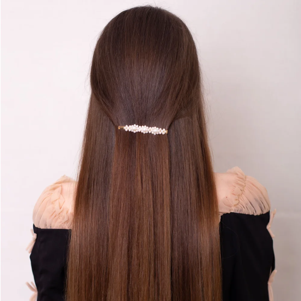 Back view of woman's long straight hair styled with a barrette while she wears an off-shoulder black top