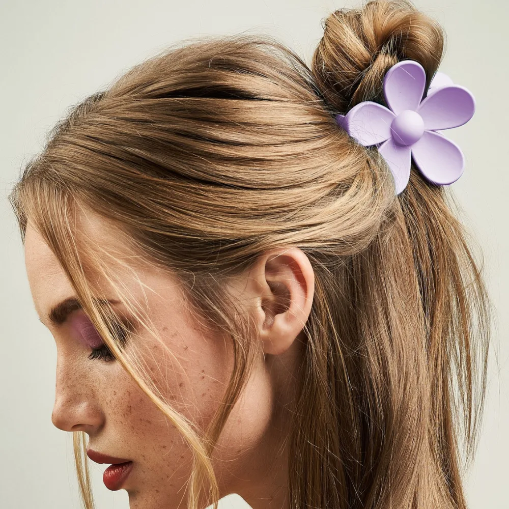 Young woman wears a purple flower clip in her half-up hairstyle, one of the best hair loss hairstyles for thinning hair on crown