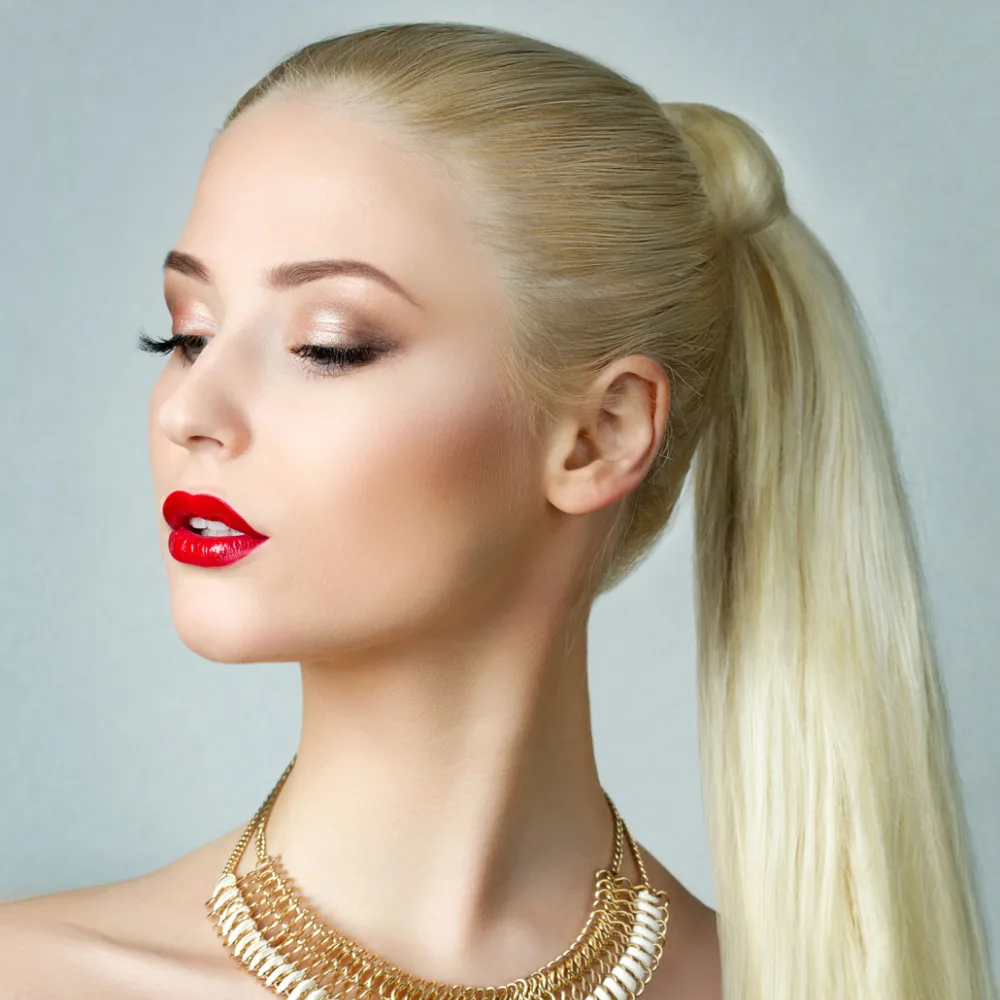 Blonde woman looks down with gold necklace and chic ponytail hairstyle with long straight hair