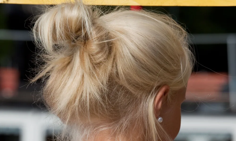 Close-up back view of a woman with blonde hair modeling one of the easiest ponytail hairstyles with a tucked-under ponytail featuring a few loose strands