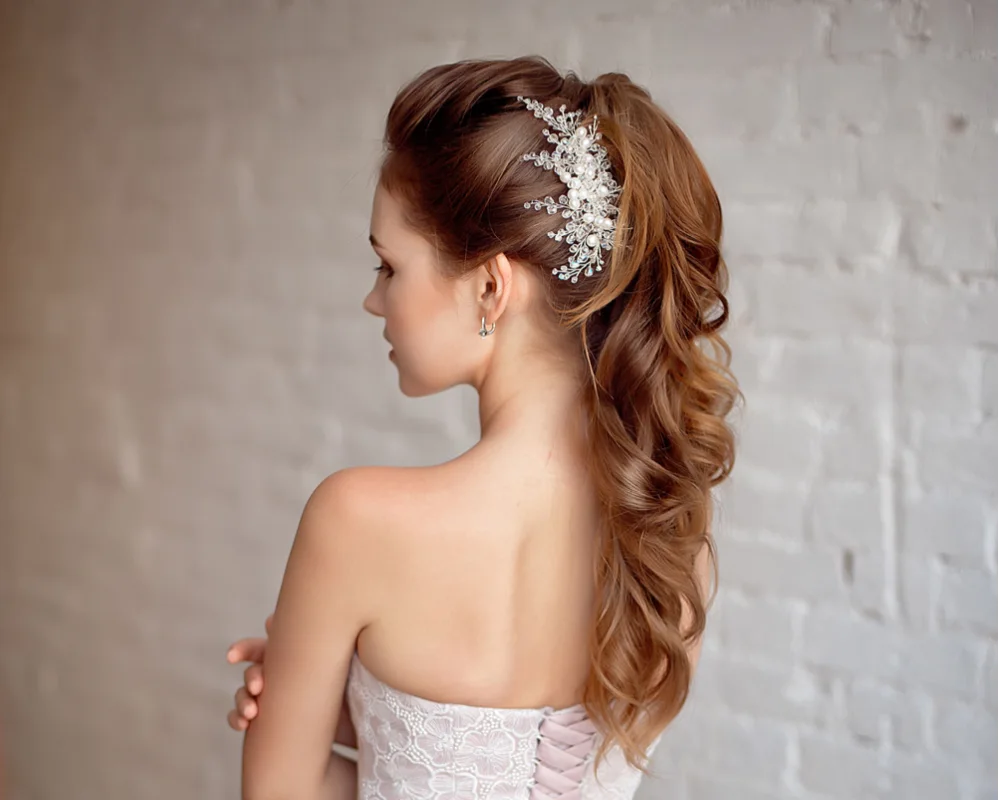 Back side view of young brunette woman wearing a curly ponytail hairstyle for homecoming with a jeweled clip accessory
