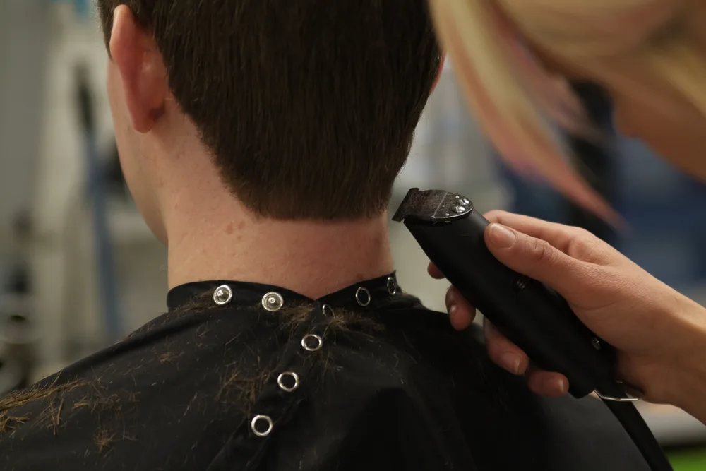 Close up back view of a man getting a haircut with clippers from a blonde woman for a piece showing the best low maintenance haircuts for men