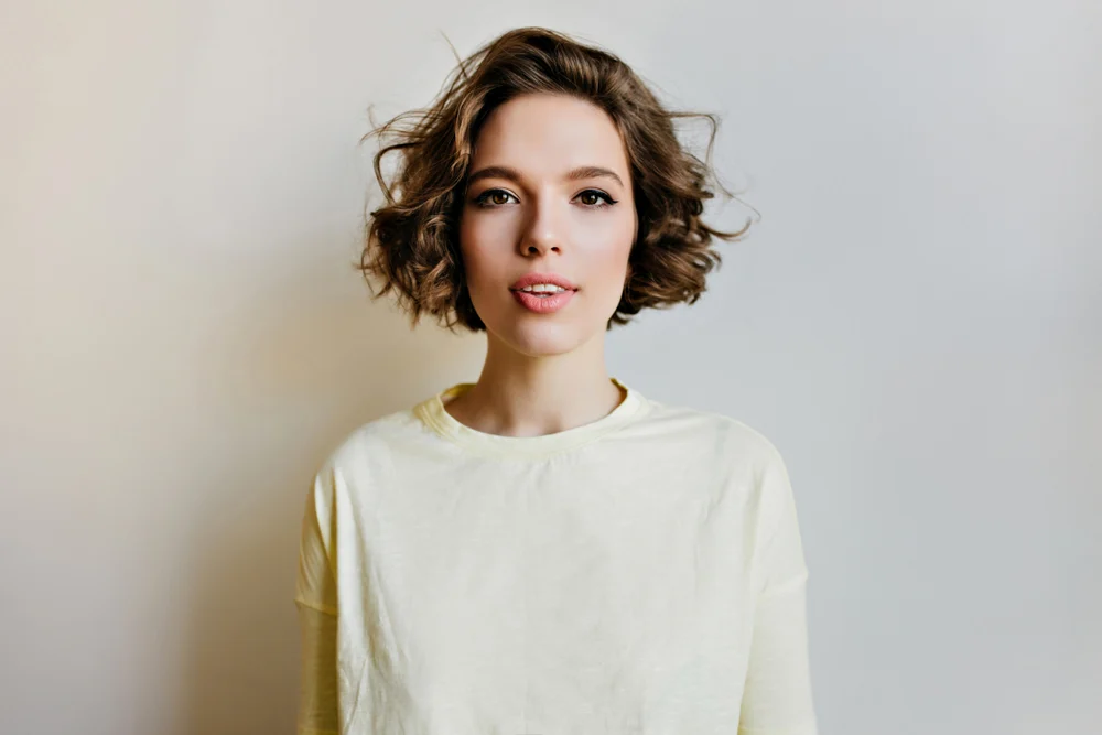 Portrait of brown haired woman in a white sweater wearing a layered curly bob as one of the top low maintenance haircuts for women